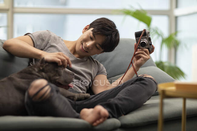 Молодий китайський чоловік пестить собаку і тримає камеру в руці — стокове фото