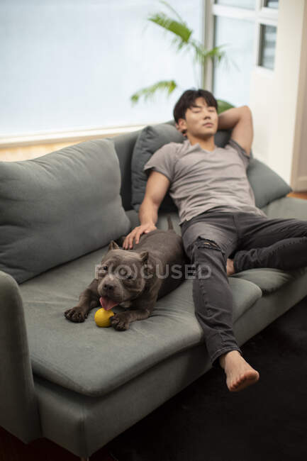 Jeune homme chinois dormant sur le canapé avec chien — Photo de stock