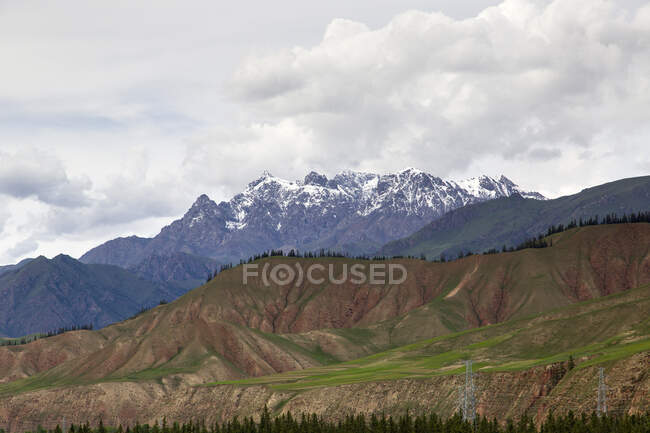 Green hills and snowy rocks under cloudy sky, China — Stock Photo