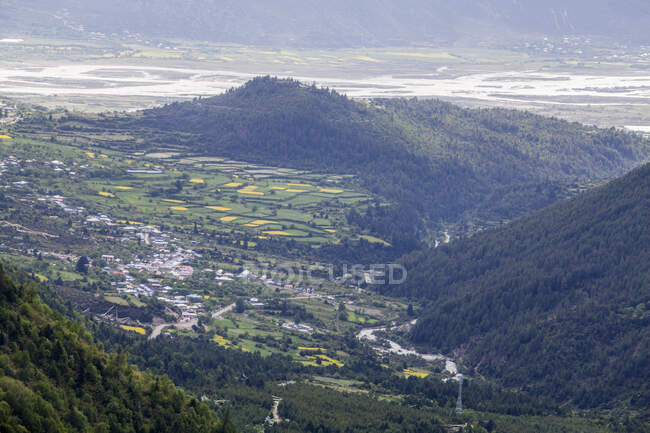 Village de vallée avec des bâtiments lointains entourés de collines verdoyantes — Photo de stock