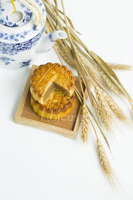 Mooncakes and teapot with spikelets on white table — Stock Photo