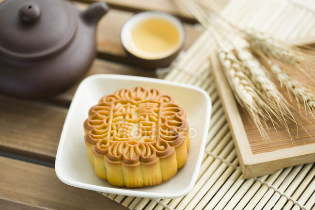 Mooncake and tea in cup and teapot with spikelets on wooden table — Stock Photo