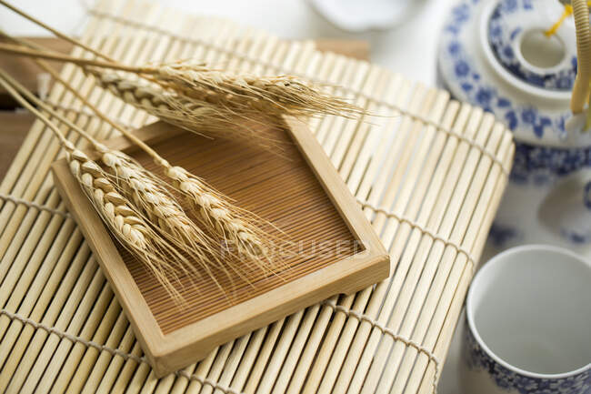 Espiguillas de trigo en la superficie de madera y tazas de té y tetera en el fondo - foto de stock