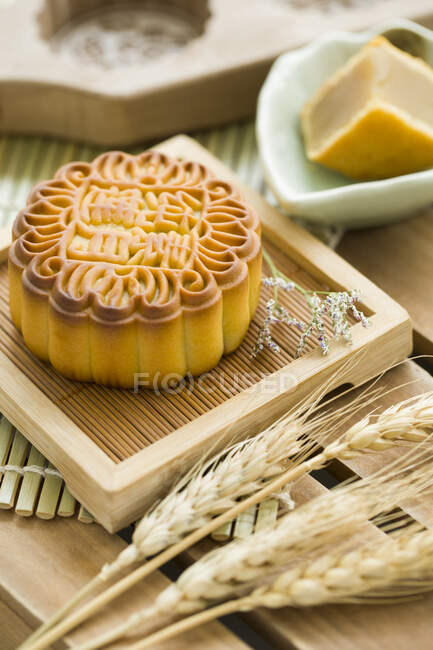 Лунный торт на маленьком деревянном подносе с цветами и пшеничными шипами на столе — стоковое фото
