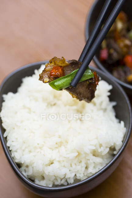 White rice in bowl and beef with chili in chopsticks — Stock Photo