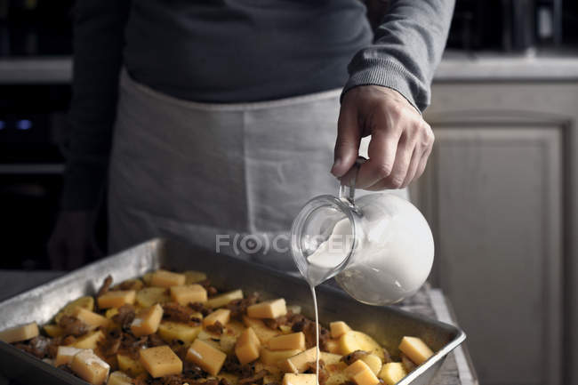 Adding cream in the baking tray with ingredients for tartiflette — Stock Photo