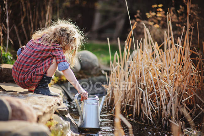 Ragazza in abito scozzese raccogliendo acqua dallo stagno in giardino primaverile — Foto stock