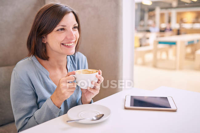 Belle femme mature souriant tout en tenant son café à table — Photo de stock