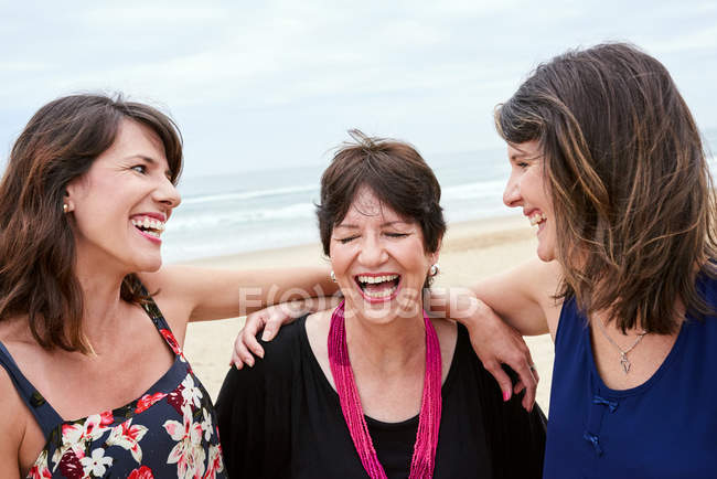 Madre e hijas riendo felizmente juntas en la playa - foto de stock