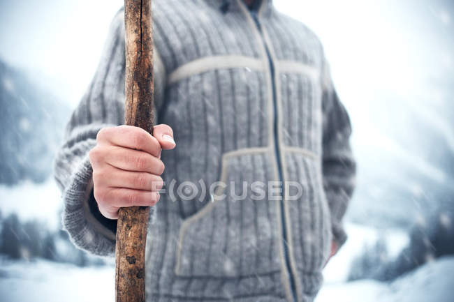 Hombre sosteniendo palo de madera en el frío invierno mientras nieva - foto de stock