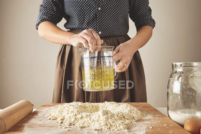 Femme mélangent l'eau d'huile d'olive dans la tasse de mesure au-dessus de la pâte — Photo de stock