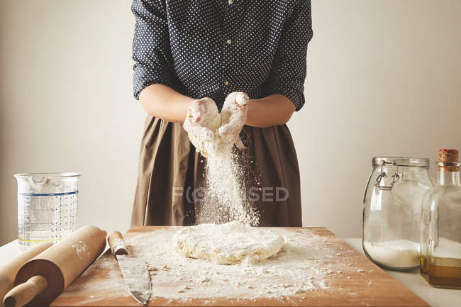 Femme ajoute de la farine à la pâte sur une table en bois — Photo de stock