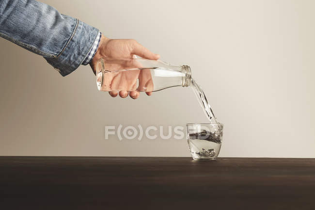 Mão derrama água limpa de garrafa em copo — Fotografia de Stock