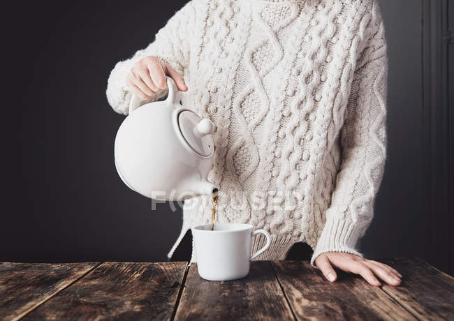 Woman in white sweater pours hot tea from big ceramic teapot — Stock Photo