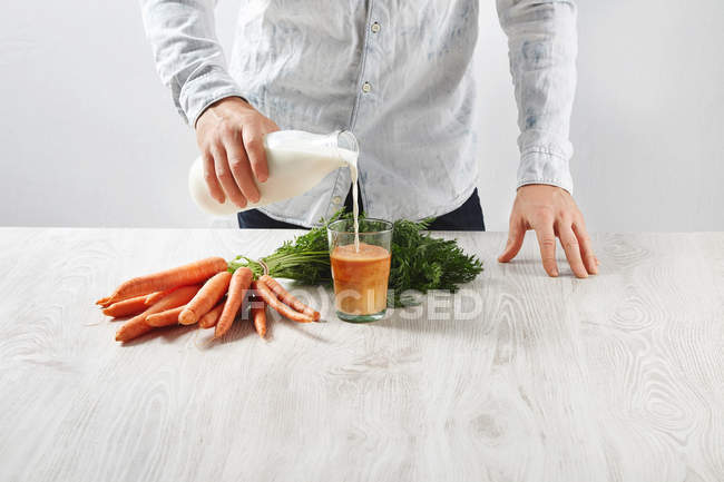 Homme verse du lait au verre avec du jus de carotte — Photo de stock