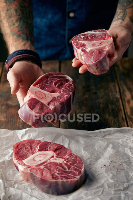 Two steaks in tattooed hands and other on craft paper — Stock Photo