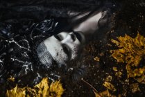 Retrato de mujer con maquillaje de fantasía acostada en el suelo con hojas de otoño - foto de stock