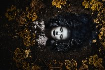 Porträt einer Frau mit Fantasie-Make-up, die mit Herbstblättern auf dem Boden liegt — Stockfoto