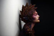Seitenansicht einer jungen Frau mit Fantasie-Make-up-Kunst und Blumenschmuck — Stockfoto