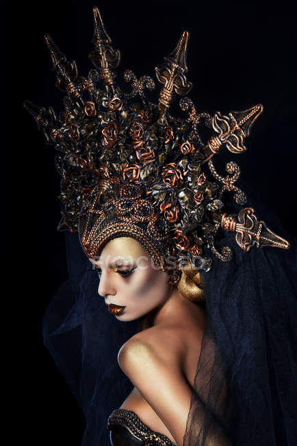 Woman with fantasy makeup wearing large crown and posing at camera ...