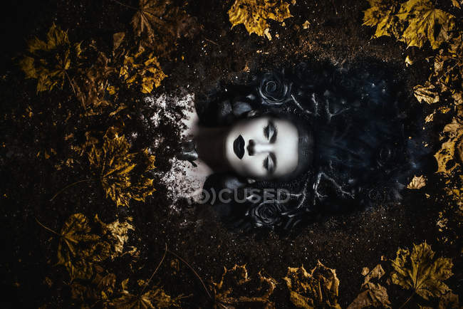 Portrait of woman with fantasy makeup lying on ground with autumn leaves — Stock Photo