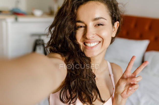 POV de heureuse Caucasienne jolie jeune femme brune en intérieur posant sur un appareil photo smartphone en prenant des photos selfie et en souriant. Joyeux positif belle dame prend une photo d'elle-même à la maison. Concept de gros plan — Photo de stock