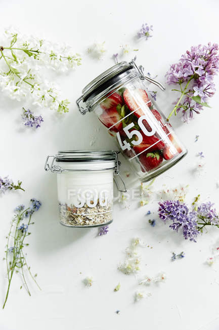 Strawberries and cereals in jars and spring flowers — Stock Photo