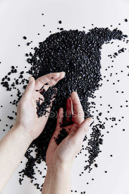 Menschenhände und schwarze Bohnen — Stockfoto
