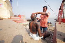 Gente afeitándose cerca del río Ganges en el casco antiguo de Varanasi . - foto de stock