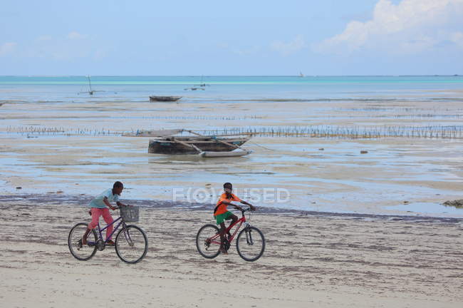Niños Montar bicicletas en la playa Zanzíbar - foto de stock