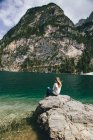 Молода жінка сидить на скелі біля озера — стокове фото