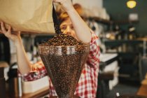 Mujer vertiendo granos de café en una tolva amoladora - foto de stock