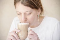 Retrato de una mujer bebiendo café con leche . - foto de stock