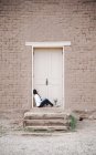 Mulher sentada no chão fora da porta da frente de um edifício . — Fotografia de Stock