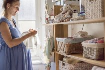Mujer embarazada ordenando ropa de bebé - foto de stock