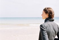Женщина в серой куртке, смотрящая на пляж — стоковое фото
