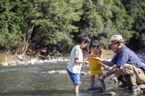Father and two children by a river. — Stock Photo