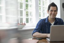 Man using laptop seated by window. — Stock Photo