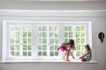 Schwestern spielen an einem großen Fenster. — Stockfoto