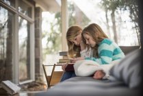 Two girls reading book on sofa. — Stock Photo