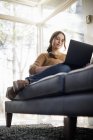 Жінка сидить на дивані і дивитися на ноутбук — стокове фото