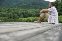 Uomo seduto su un molo di legno vicino a un lago — Foto stock
