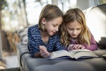 Girls looking at book on sofa — Stock Photo