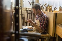 Möbelrestaurator sitzt mit Smartphone — Stockfoto
