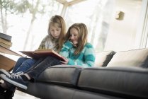 Two girls reading a book on sofa — Stock Photo