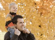 Father and son under autumn leaves. — Stock Photo