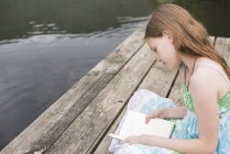 Fille lecture par un lac — Photo de stock