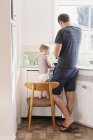 Homem de pé em uma cozinha com o filho — Fotografia de Stock