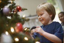 Boy placing Christmas baubles on tree — Stock Photo