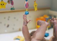 Baby girl reaching up to a colourful mobile — Stock Photo